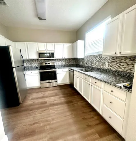 a kitchen with granite countertop a sink a stove a refrigerator and white cabinets