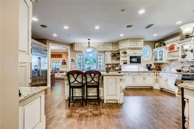 a kitchen with stainless steel appliances kitchen island granite countertop a refrigerator a stove a dining table and chairs with wooden floor