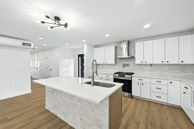 a kitchen with stainless steel appliances kitchen island granite countertop a stove a sink a refrigerator and white cabinets with wooden floor