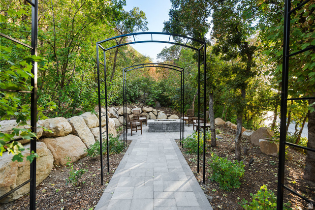 1141 South Oak Leaf Lane Springville, UT 84663 - Photo 114 of 147 Outdoor patio featuring a stone-paved walkway, multiple metal arbors, natural rock retaining walls, a built-in fire pit, and extensive natural landscaping