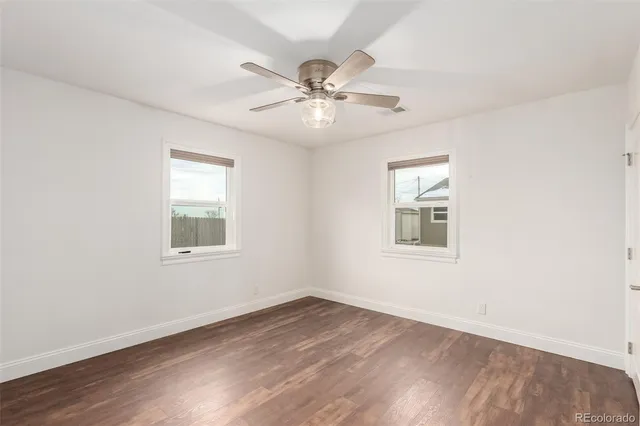 an empty room with wooden floor ceiling fan and windows