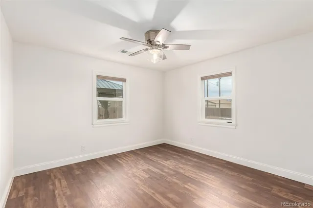an empty room with wooden floor ceiling fan and windows