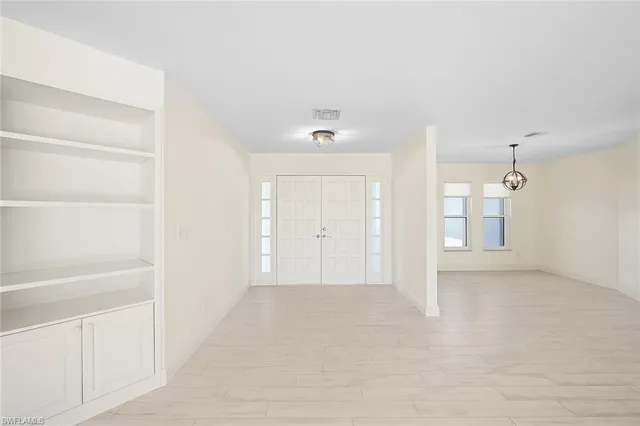 an empty room with wooden floor chandelier and windows