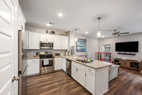 a kitchen with stainless steel appliances kitchen island granite countertop a stove top oven a sink dishwasher a refrigerator and a dining table with wooden floor