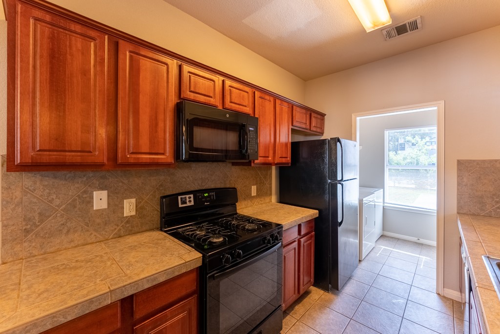 3000 Govalle Avenue, Unit B Austin, TX 78702 - Photo 11 of 26 Kitchen with black appliances, light tile patterned floors, tasteful backsplash, and tile countertops