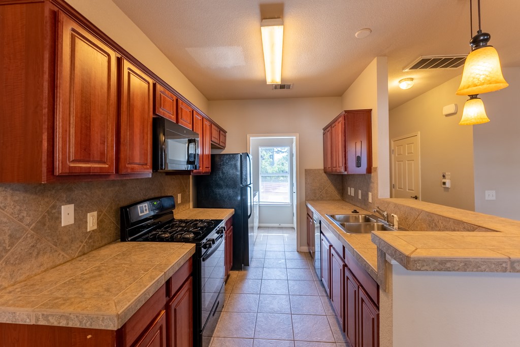 3000 Govalle Avenue, Unit B Austin, TX 78702 - Photo 9 of 26 Kitchen featuring black appliances, a peninsula, decorative backsplash, decorative light fixtures, and light tile patterned flooring