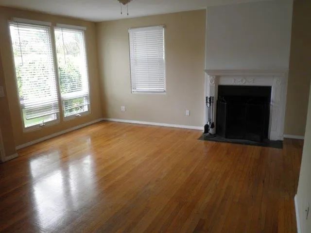 a view of an empty room with wooden floor and a fireplace