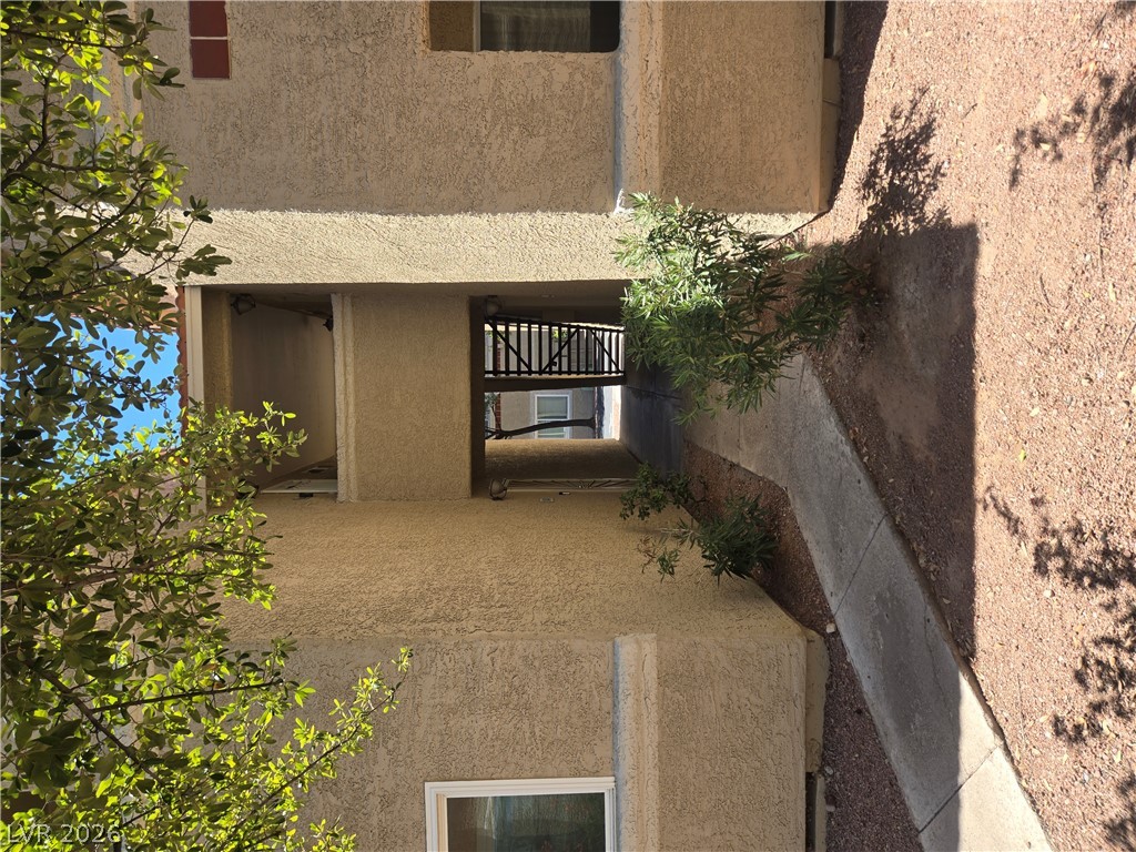 7200 West Pirates Cove Road, Unit 2047 Las Vegas, NV 89145 - Photo 16 of 17 Concrete pathways lead to the building's covered entrance, framed by mature trees and landscaped gravel.