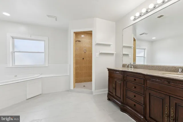 a bathroom with a granite countertop double vanity sink a mirror and a bathtub