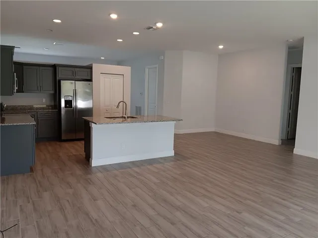 an empty room with wooden floor and kitchen view