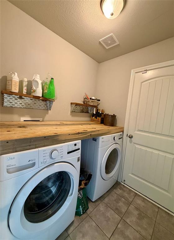619 Mansfield Road Cleburne, TX 76031 - Photo 12 of 19 Functional laundry area featuring a wood-finish countertop over appliances, tiled flooring, and a paneled door leading to the 1 car garage