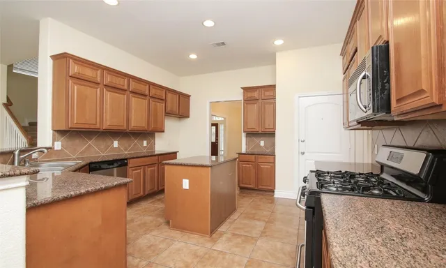 a kitchen with stainless steel appliances granite countertop a stove top oven a sink a refrigerator and cabinets