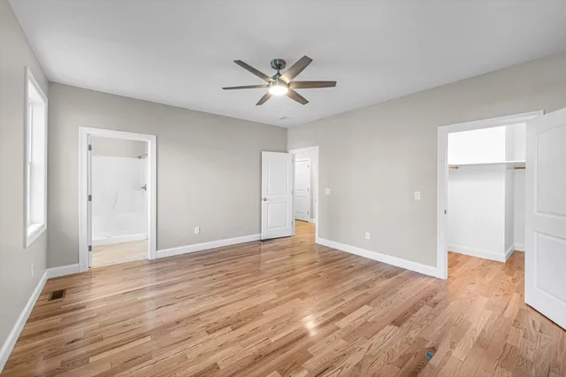 a view of an empty room with wooden floor and a ceiling fan