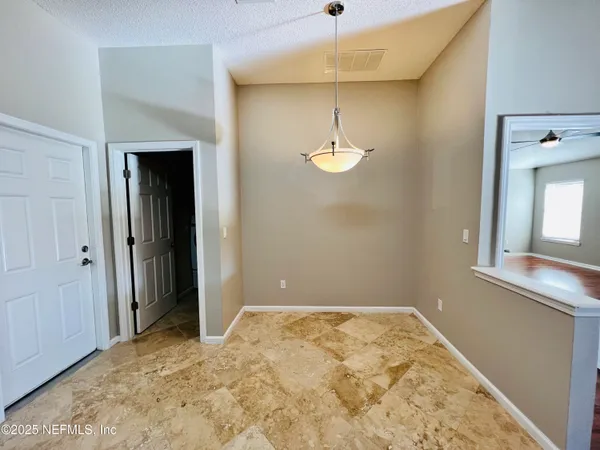 an empty room with a chandelier fan and kitchen view