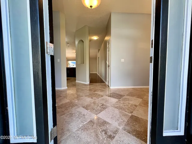 an empty room with a chandelier fan and kitchen view