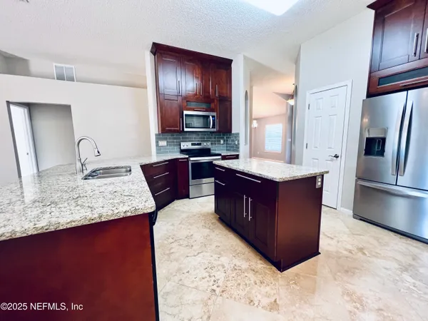 a large kitchen with kitchen island granite countertop a sink refrigerator and cabinets