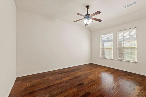 an empty room with wooden floor fan and windows