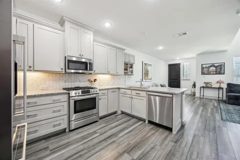 a kitchen with stainless steel appliances granite countertop a stove top oven a sink dishwasher and a refrigerator with wooden floor