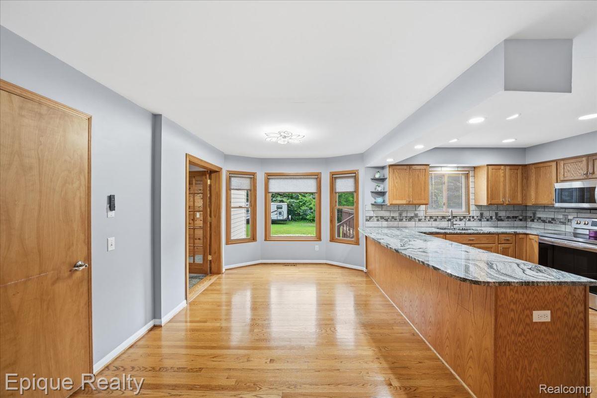 1221 Rhodes Road Lake Orion, MI 48360 - Photo 11 of 72 Kitchen and dining area featuring a U-shaped island with a stone countertop, light wood cabinetry, and wood-finish flooring