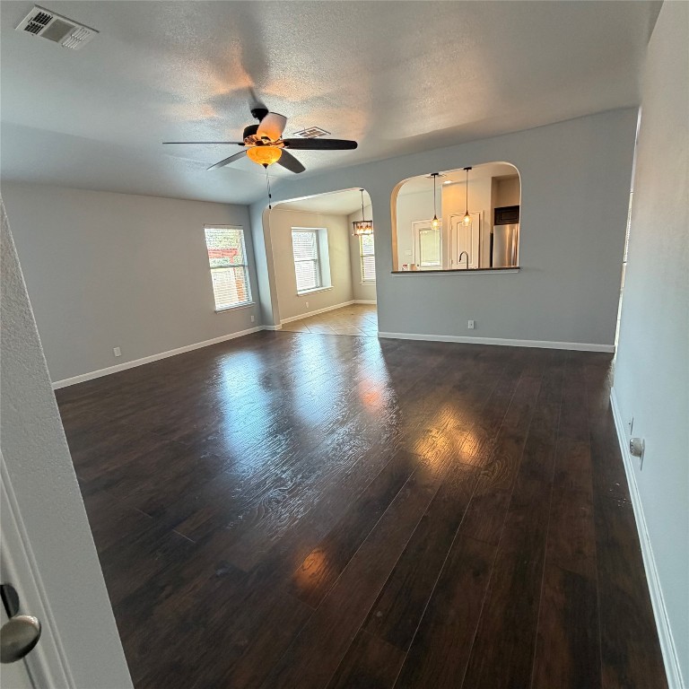 1115 Sunny Meadows Loop Georgetown, TX 78626 - Photo 11 of 36 Empty room featuring arched walkways, a ceiling fan, dark wood finished floors, and a textured ceiling