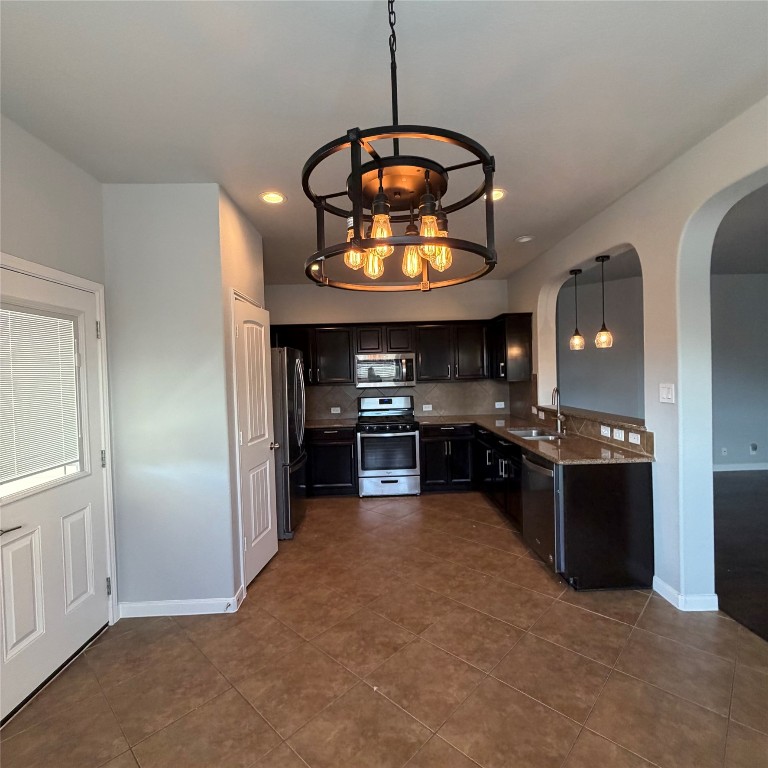 1115 Sunny Meadows Loop Georgetown, TX 78626 - Photo 25 of 36 Kitchen featuring arched walkways, appliances with stainless steel finishes, a chandelier, pendant lighting, and dark stone counters