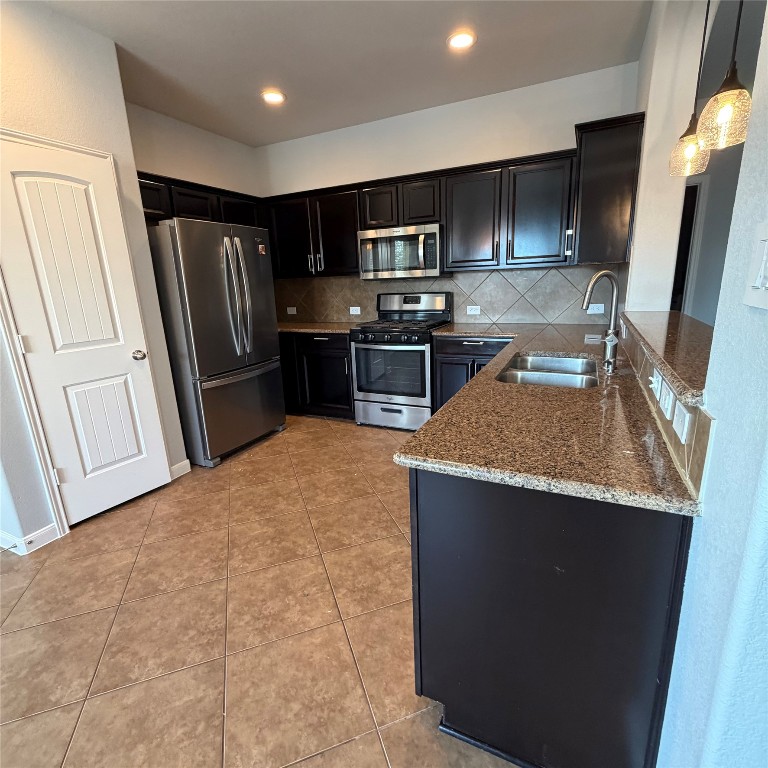 1115 Sunny Meadows Loop Georgetown, TX 78626 - Photo 26 of 36 Kitchen featuring appliances with stainless steel finishes, light stone counters, dark cabinetry, light tile patterned flooring, and backsplash