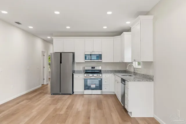 a kitchen with stainless steel appliances granite countertop a refrigerator oven a sink and white cabinets