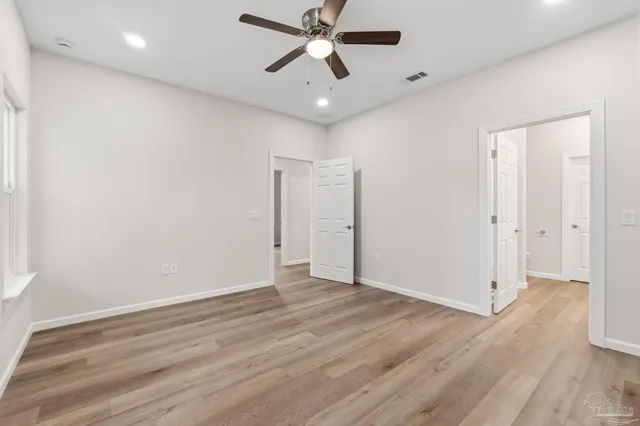 an empty room with wooden floor ceiling fan and windows