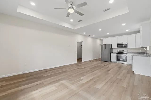 a view of an empty room with kitchen appliances and a ceiling fan
