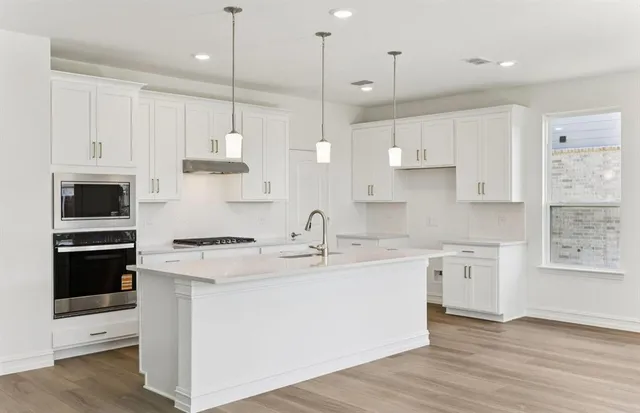 a kitchen with stainless steel appliances granite countertop a sink a stove a refrigerator and white cabinets
