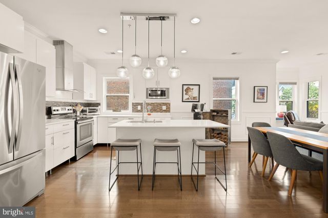 a kitchen with a dining table chairs wooden floor cabinets and appliances
