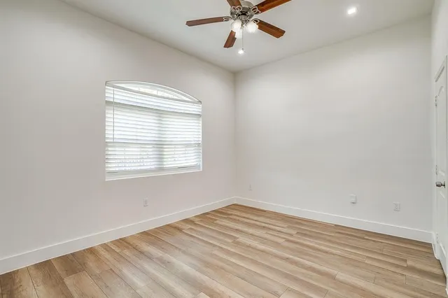 an empty room with wooden floor fan and windows