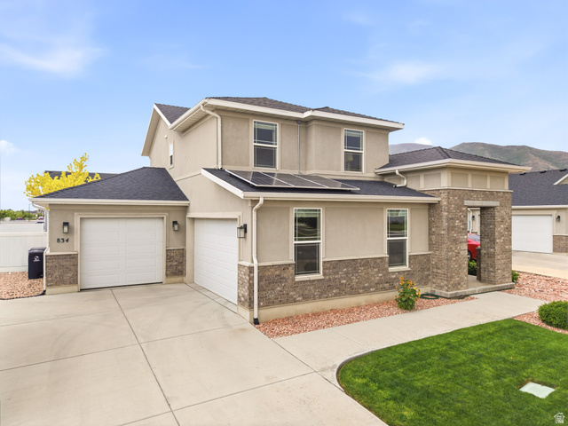 834 West 1050th Street South Springville, UT 84663 - Photo 26 of 26 Two-story stucco and brick-veneer residence featuring solar panels, multiple garage doors, concrete driveway, and a manicured lawn