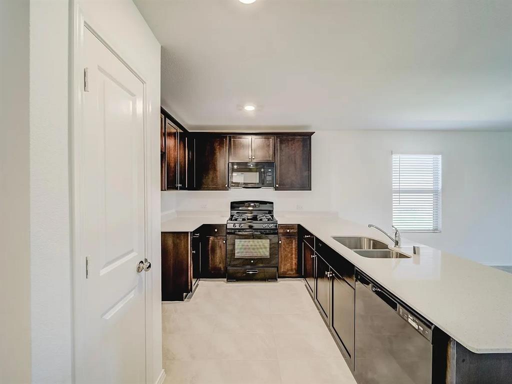 352 Sun Bluff Road Fort Worth, TX 76052 - Photo 4 of 33 Kitchen featuring dark wood cabinetry, light-toned countertops, and stainless steel appliances including a gas range and microwave