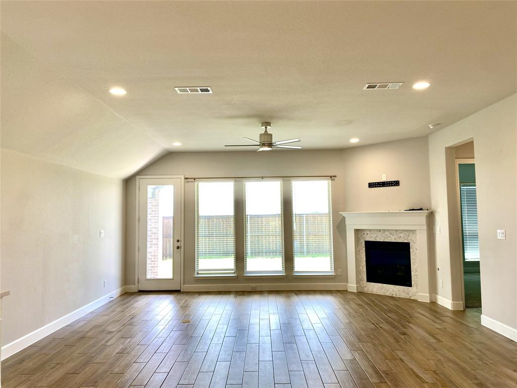 1937 Halkin Road Celina, TX 75009 - Photo 15 of 20 Spacious living area featuring wood-like tile flooring, a tiled fireplace with a white mantel, and ample natural light from multiple windows