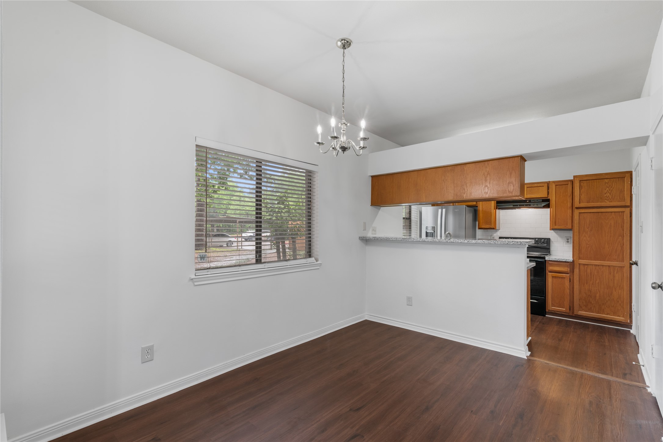 3500 Tangle Brush Drive, Unit 193 Spring, TX 77381 - Photo 5 of 26 Dining area with a large window, hardwood floors, and a modern chandelier. The space opens to a kitchen featuring granite countertops and wooden cabinets, creating a warm and inviting atmosphere.