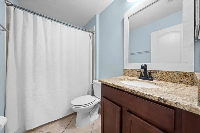 a sign that is sitting in front of a house with potted plants and large trees