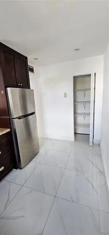 a view of a refrigerator in kitchen and an empty room