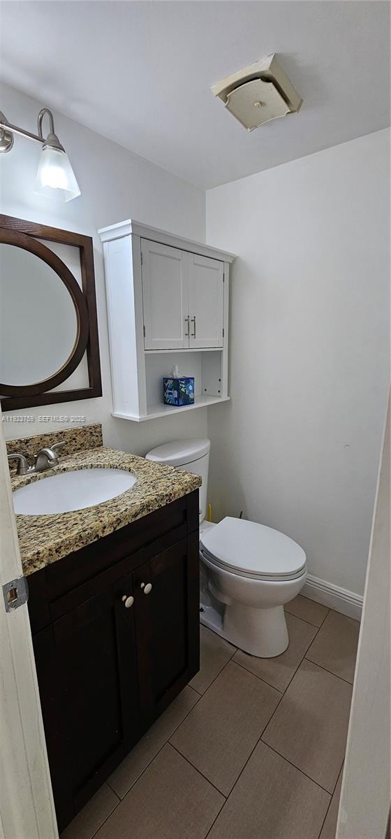 7775 Southwest 86th Street, Unit F1301 Miami, FL 33143 - Photo 10 of 20 a bathroom with a granite countertop toilet sink mirror and vanity