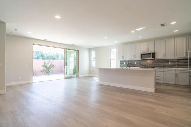 a large kitchen with stainless steel appliances granite countertop a stove a sink white cabinets and a wooden floor