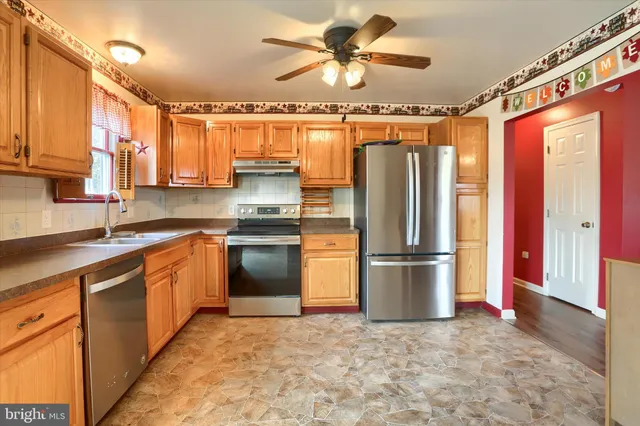 a kitchen with stainless steel appliances granite countertop a refrigerator a stove and a sink with wooden floors