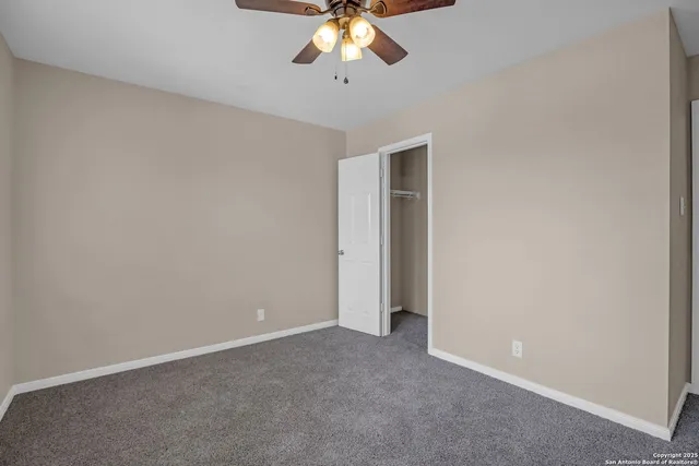 an empty room with a chandelier fan and windows