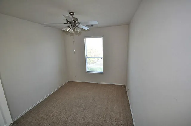an empty room that has a window and a chandelier fan