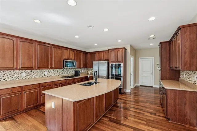 a kitchen with stainless steel appliances granite countertop a stove a refrigerator a sink and a oven with wooden floor