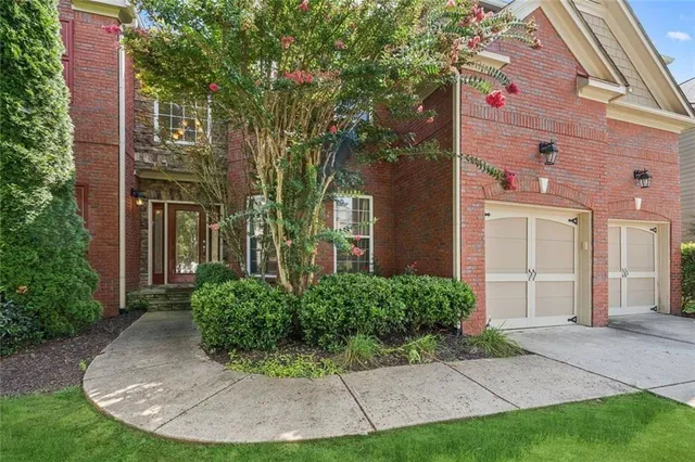 a view of a house with brick walls plants and large tree