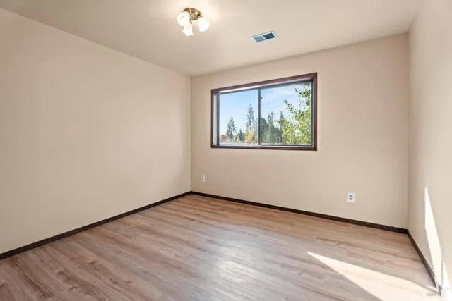 an empty room with wooden floor chandelier and windows
