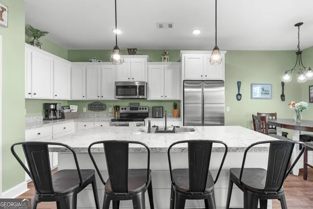 a kitchen with stainless steel appliances kitchen island granite countertop a dining table chairs refrigerator and microwave