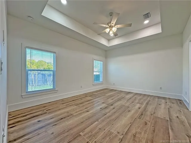 an empty room with wooden floor chandelier fan and windows