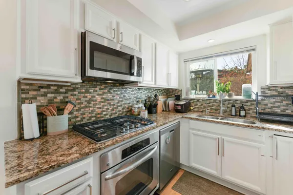 a kitchen with stainless steel appliances granite countertop white cabinets a window and a sink