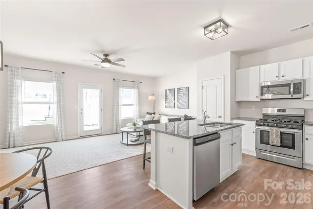 a kitchen with stainless steel appliances granite countertop a stove top oven a sink a dining table and chairs with wooden floor